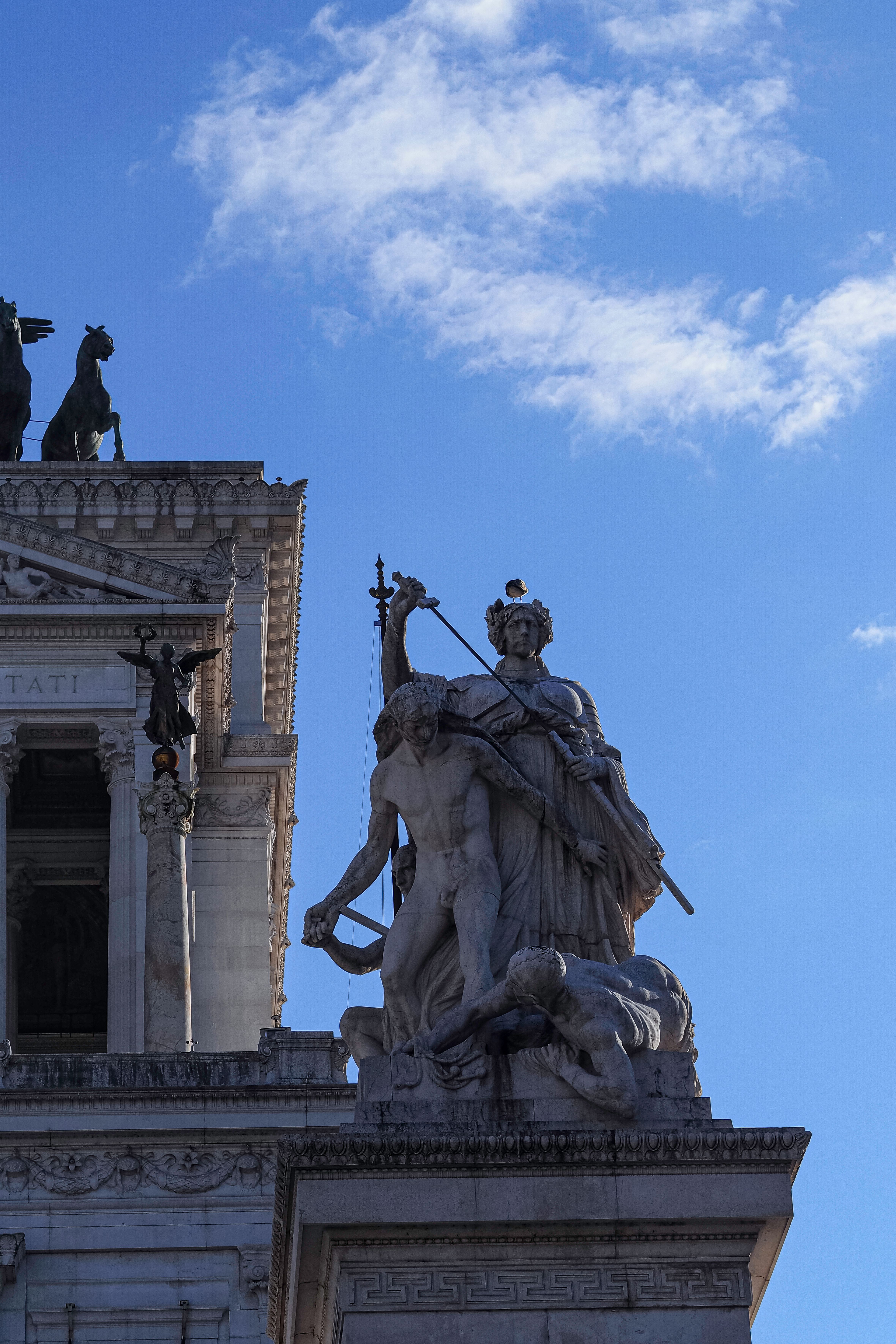 Detailed view of classical statues atop a monument in Rome, Italy, under a clear sky.
