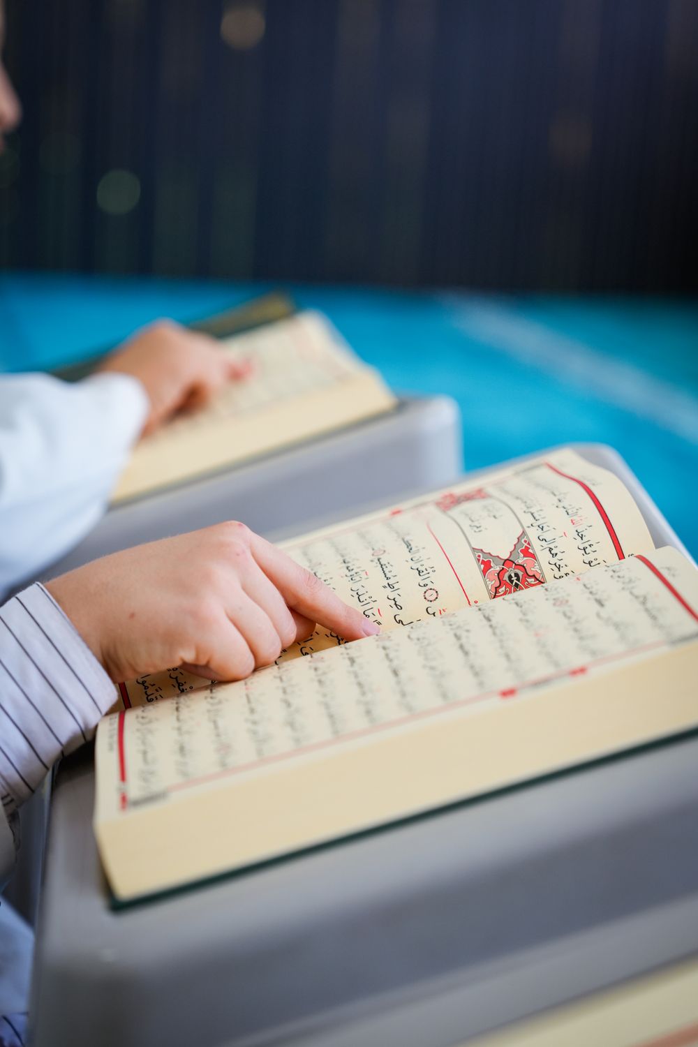 A student reading the Quran, tracing the Arabic text with his finger