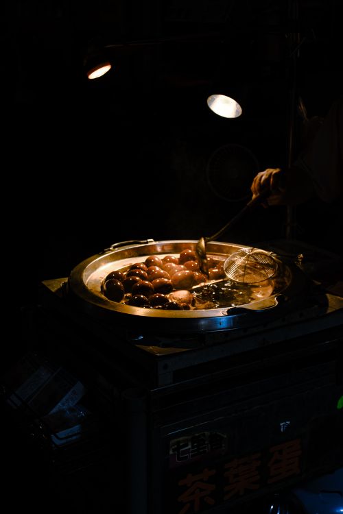 Free A street vendor prepares traditional tea eggs at night under warm lighting, focusing on rich colors and textures. Stock Photo