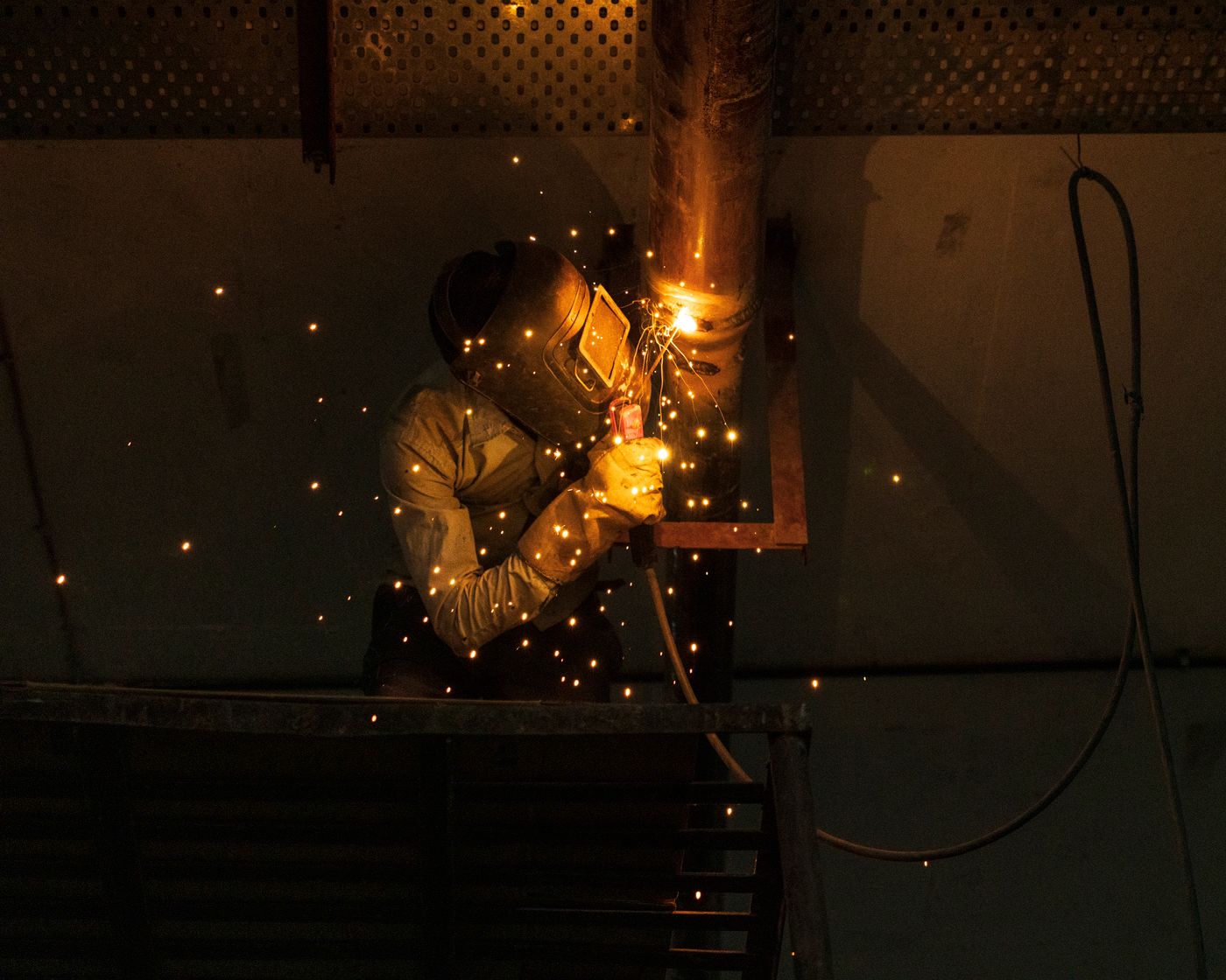 Welder running a vertical bead on an installed pipe riser indoors