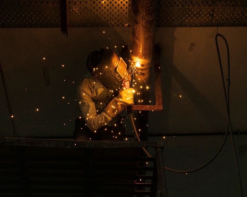 Beginner running a MIG bead on a vertical pipe joint with glowing sparks