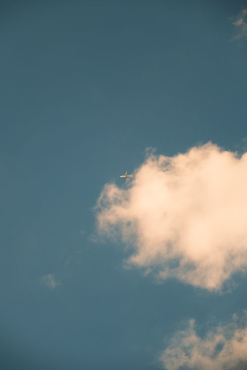 Free A high-flying airplane surrounded by fluffy clouds against a bright blue sky. Stock Photo