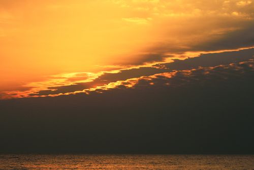 Free Vibrant sunset over ocean with dramatic clouds and warm colors. Stock Photo