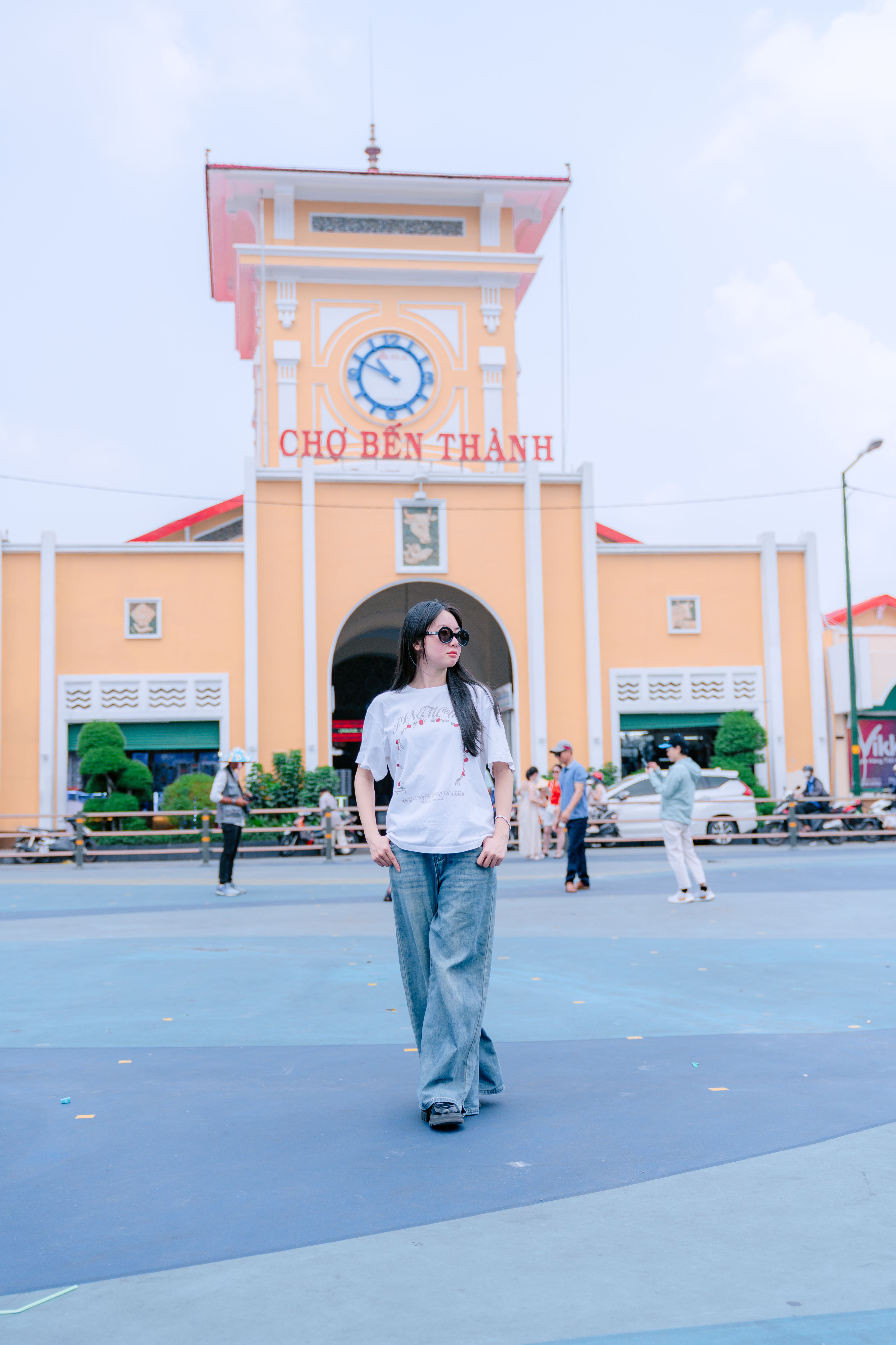 A woman in casual attire walking outdoors in front of Ben Thanh Market in Ho Chi Minh City.
