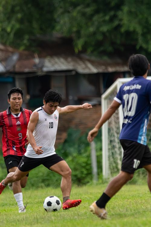 Free Players compete in an intense football match on a lush green field in Myawaddy, Myanmar. Stock Photo