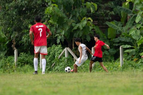 Free Soccer players in action during a local match in Myawaddy, Myanmar with lush greenery in the background. Stock Photo