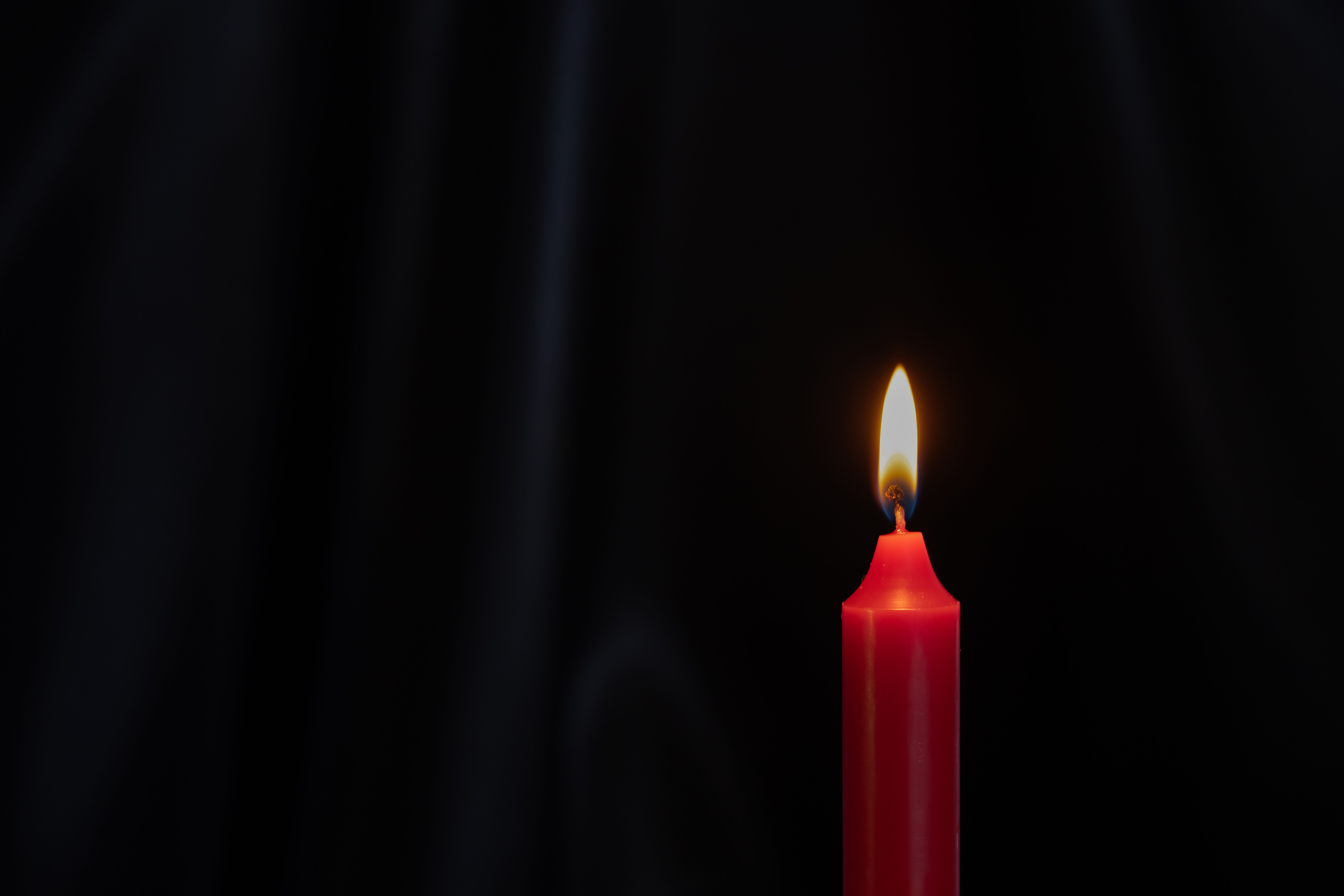 Fotomural Una vela roja ardiendo con una llama brillante sobre un fondo negro, creando un ambiente sereno.