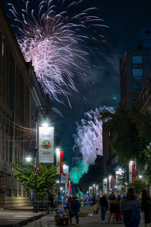 Free Fireworks light up the night sky above a lively street in Mexico City, showcasing urban night festivities. Stock Photo