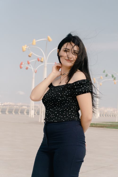 Free Young woman stands outdoors on a sunny day by the Baku promenade with wind-blown hair. Stock Photo