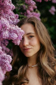 Young woman smiling amidst blooming lilac flowers, capturing a serene moment