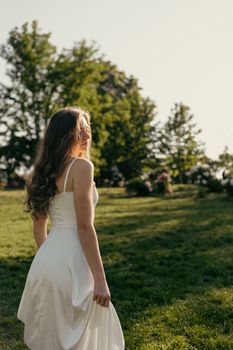 A woman in a white dress enjoys the warm sunlight in a serene park setting.