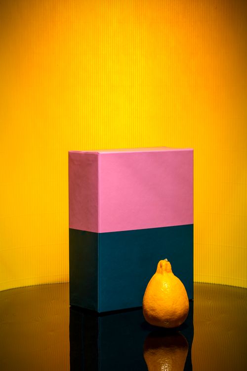 Free A striking still life of a lemon and colorful box against a bright yellow background. Stock Photo