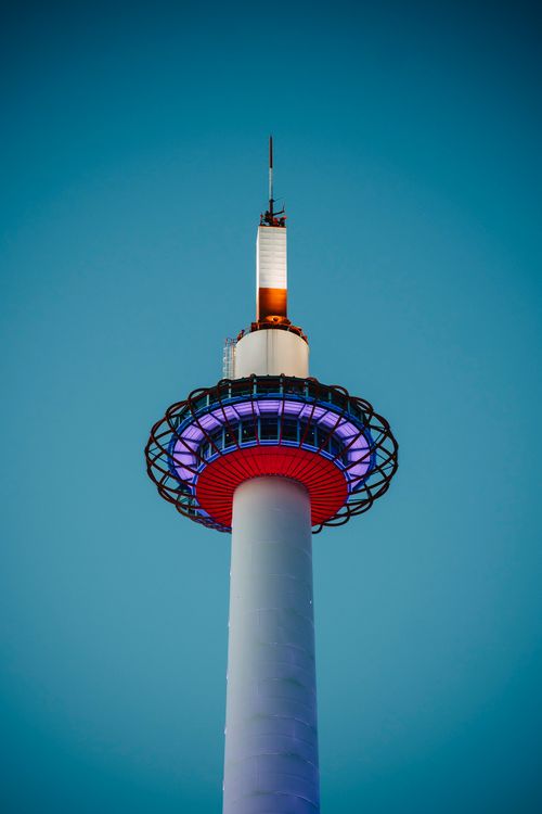 Free A stunning view of Kyoto Tower lit up in vibrant colors against a clear blue sky. Stock Photo