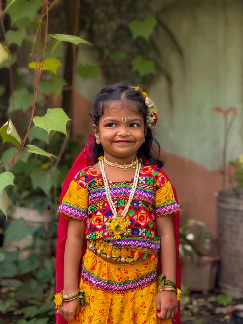 Free A joyful child in vibrant traditional Indian attire, standing outdoors surrounded by greenery. Stock Photo
