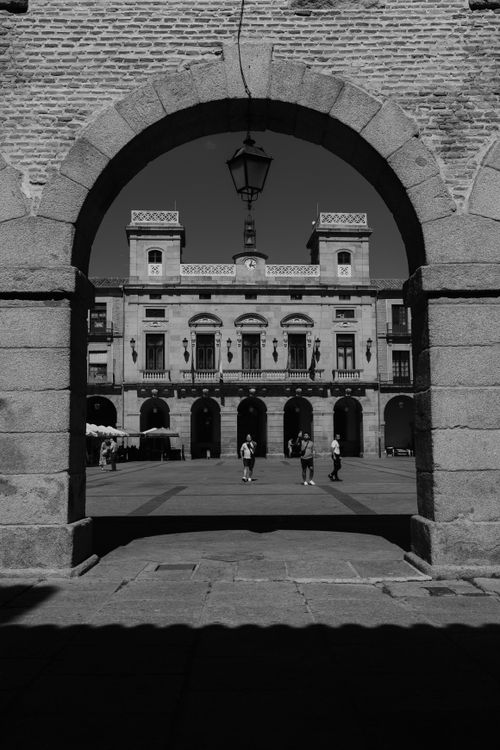 Free Black and white view of Ávila's historic plaza framed by a stone arch, capturing architectural grandeur. Stock Photo