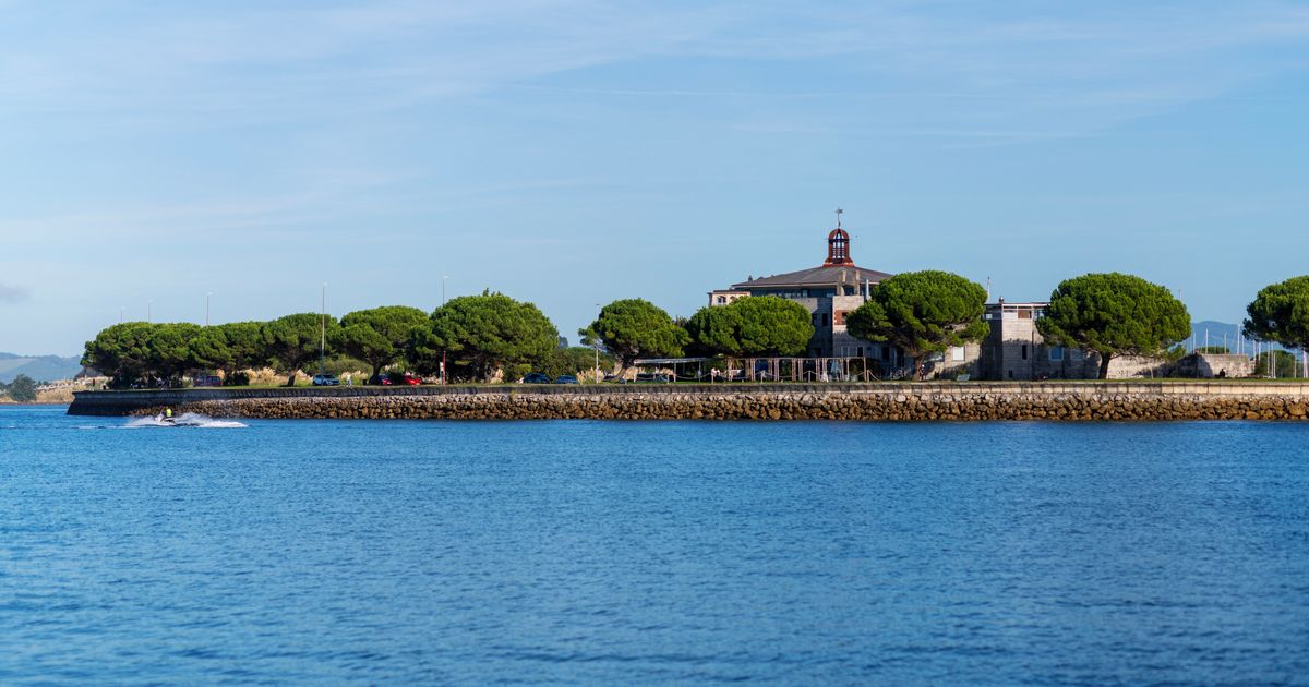Paisagem costeira serena com arquitetura histórica e vegetação exuberante à beira-mar.