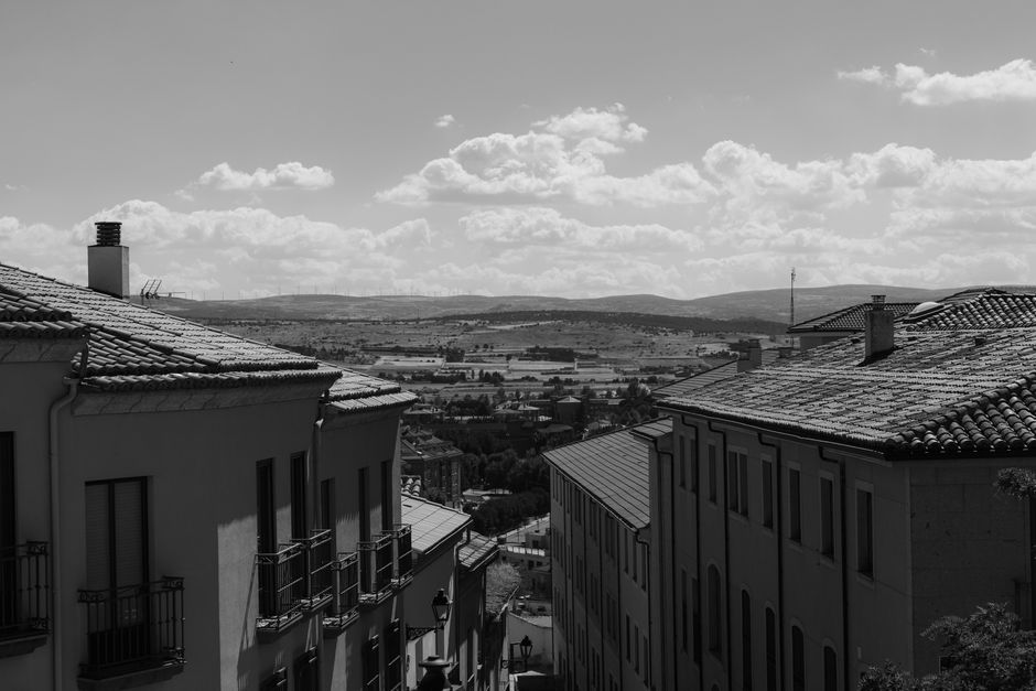 Black and white photograph showcasing the rooftops of Ávila with a scenic landscape.
