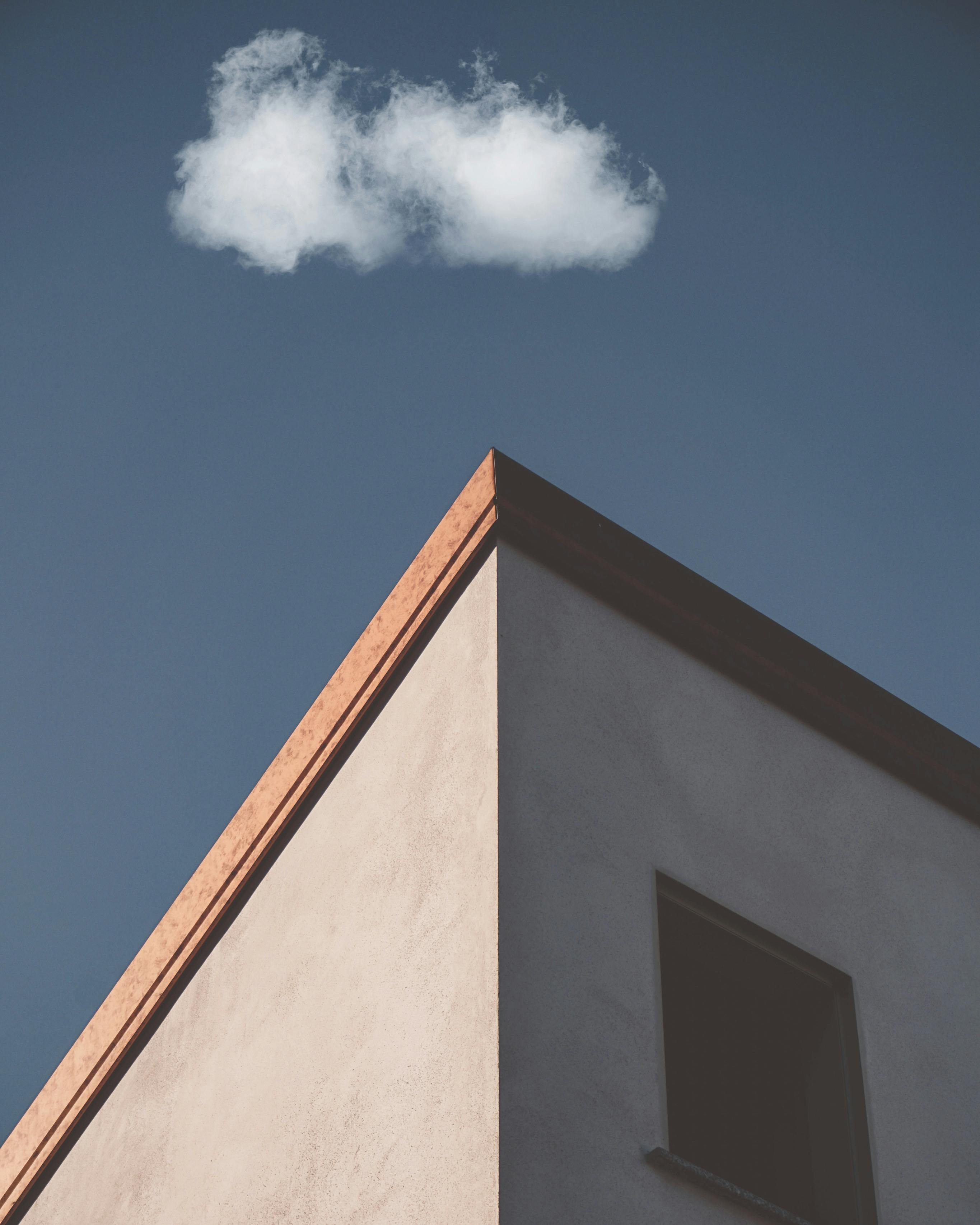Free A minimalist building corner under a blue sky with a solitary cloud. Stock Photo