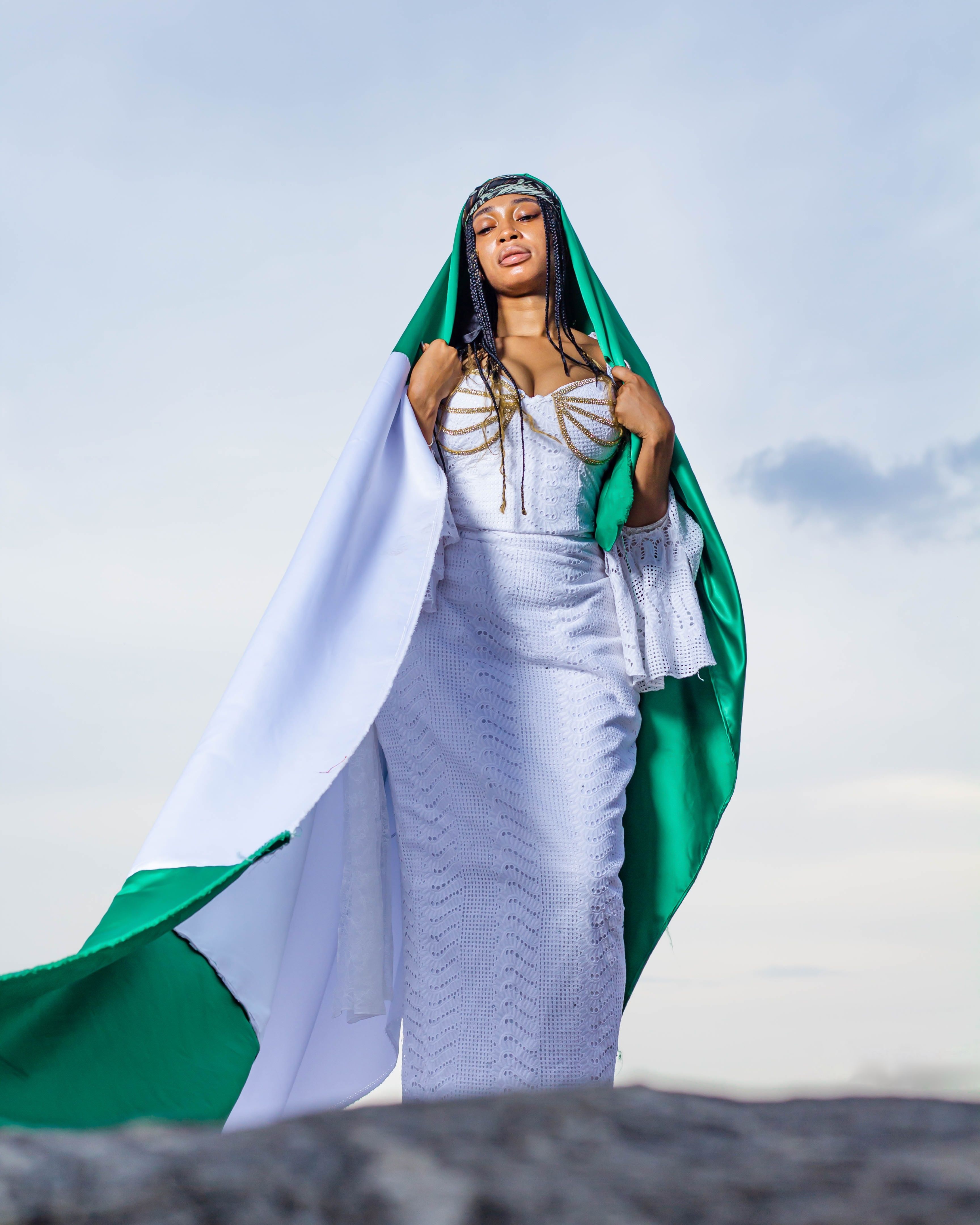 Woman in white traditional dress with flag standing outdoors, embodying cultural pride.