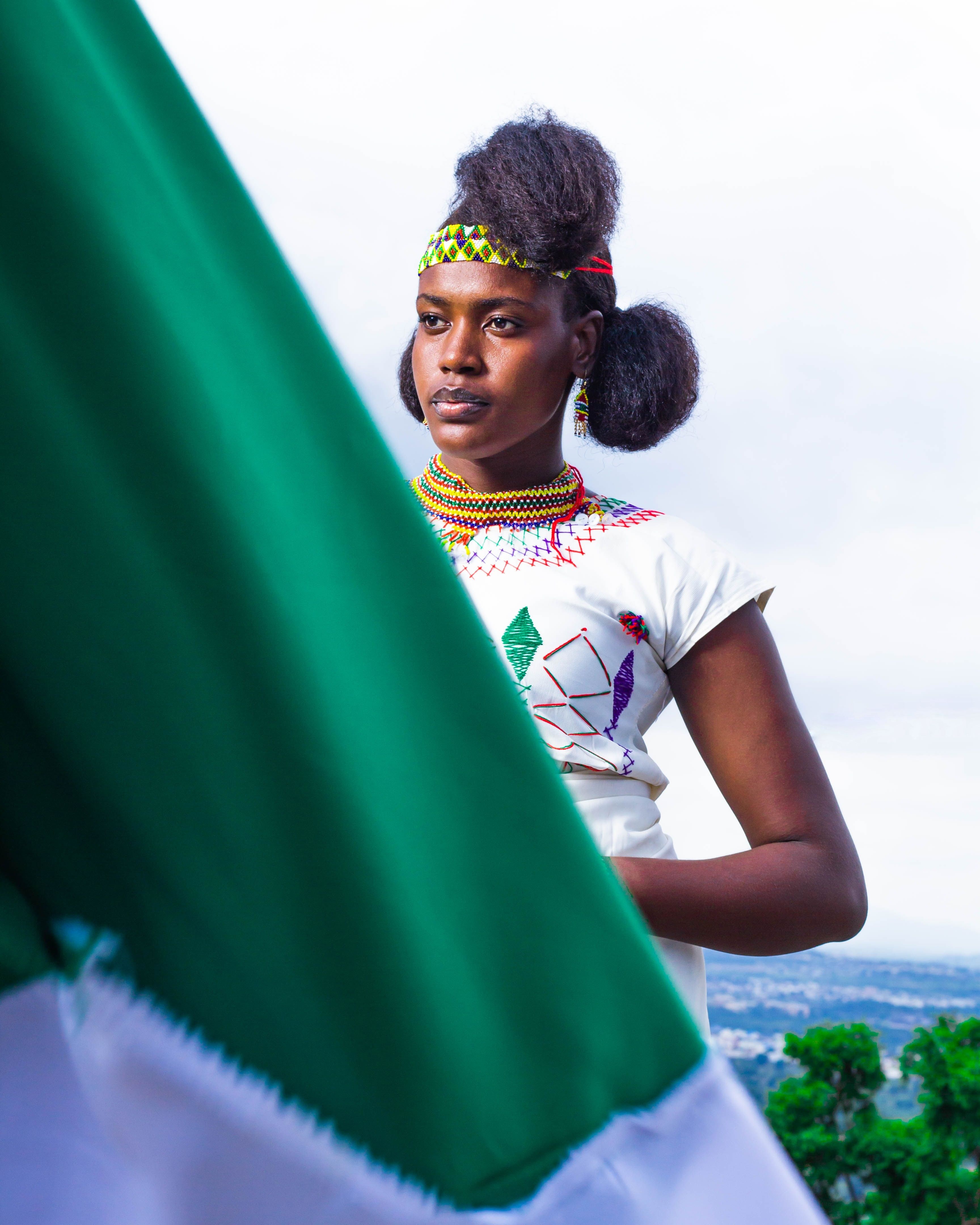 A woman in traditional African attire with vivid beadwork and colorful patterns, standing outdoors.