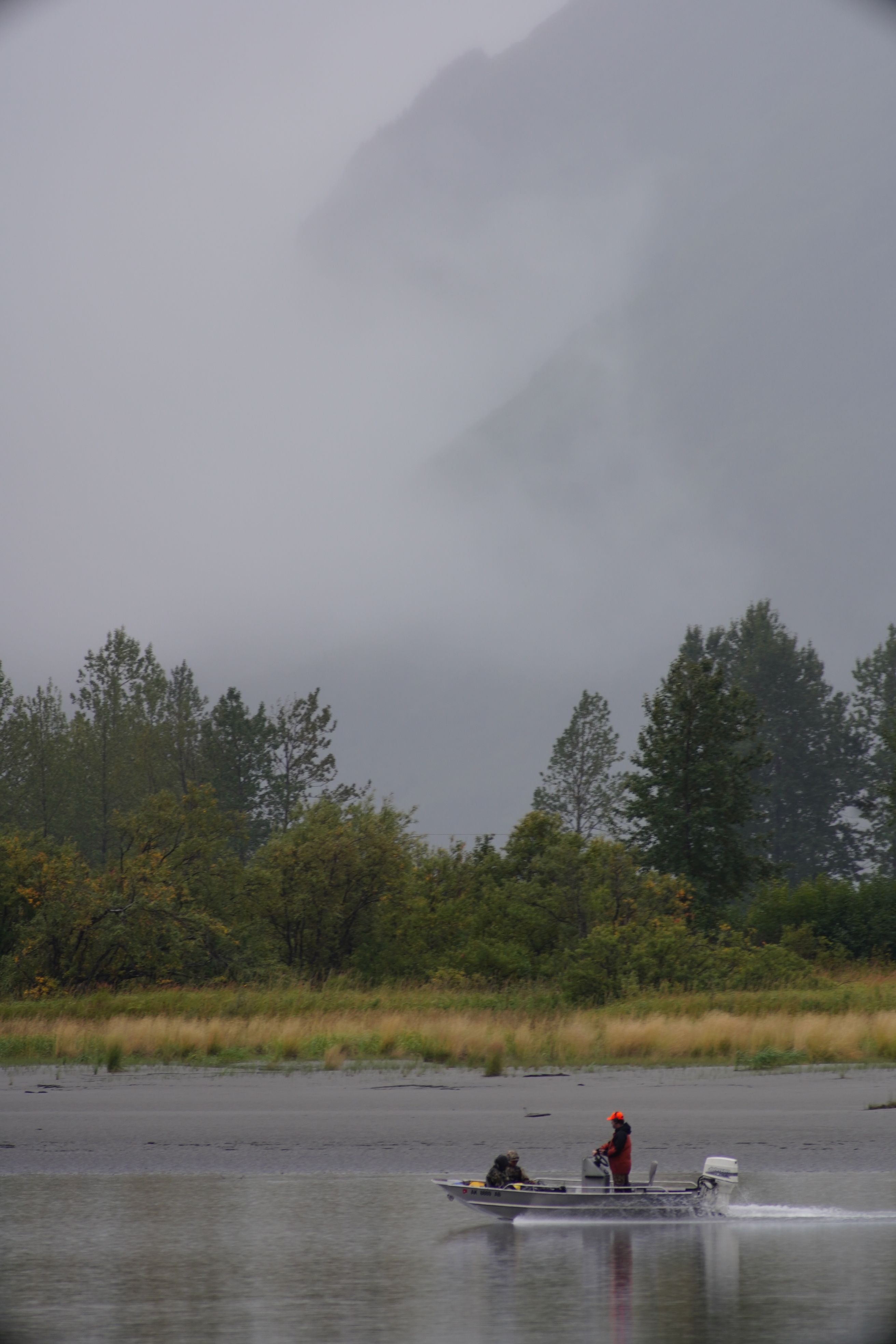 A solitary fisherman navigates a riverboat in foggy Anchorage, Alaska, showcasing serene wilderness.