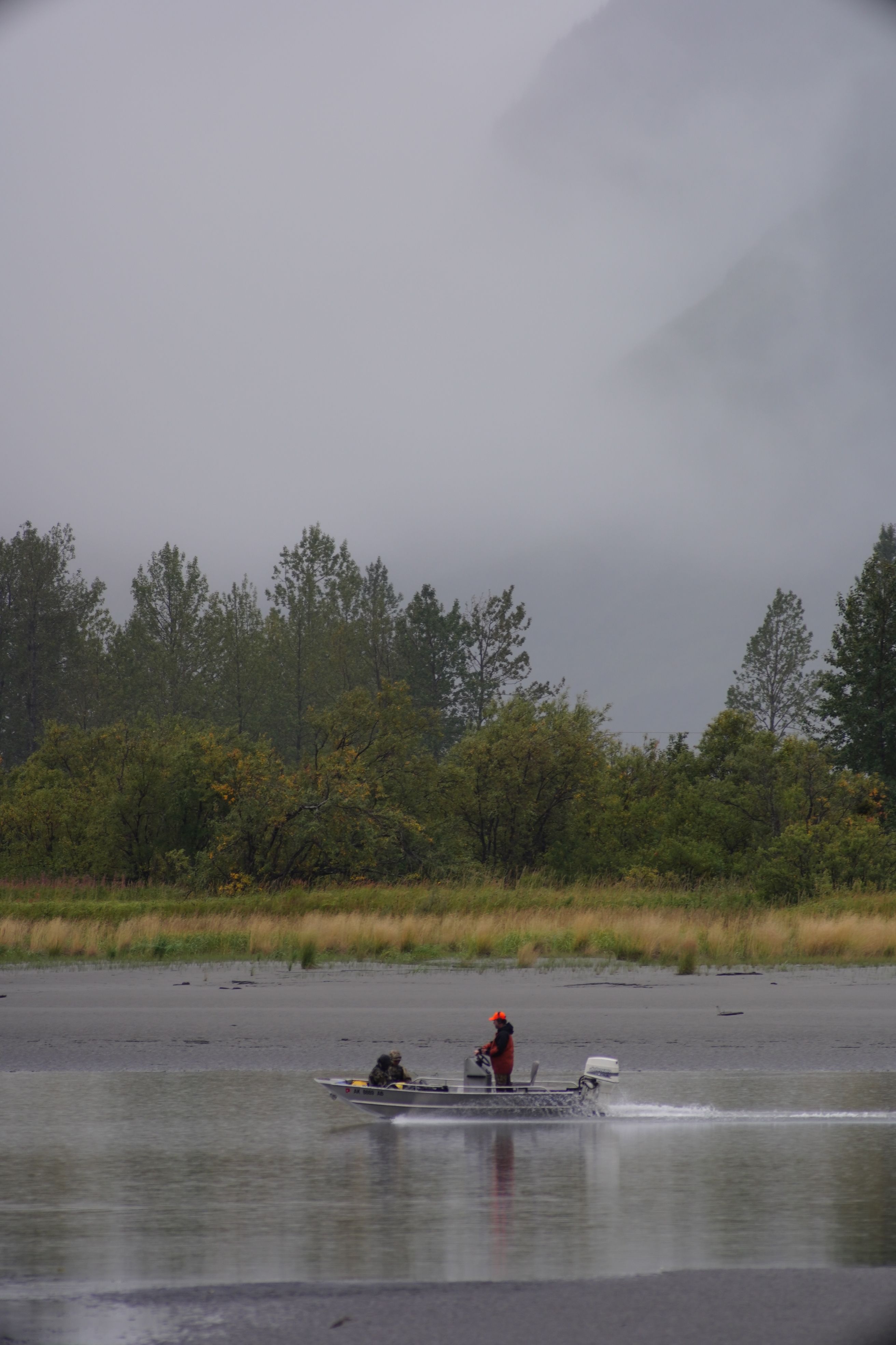 Photograph of a boat navigating Alaskan waters amidst mist and lush greenery.