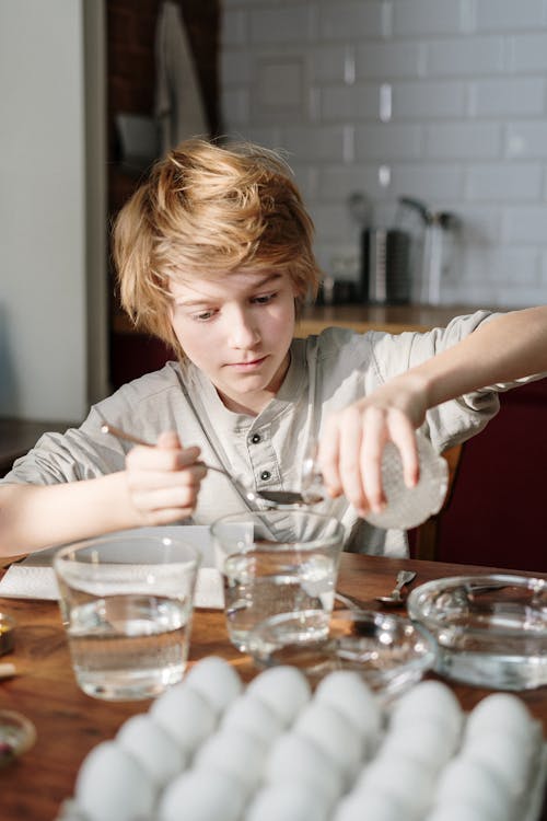 Boy in Grey Shirt Holding Clear Glass Pouring Liquid on Spoon