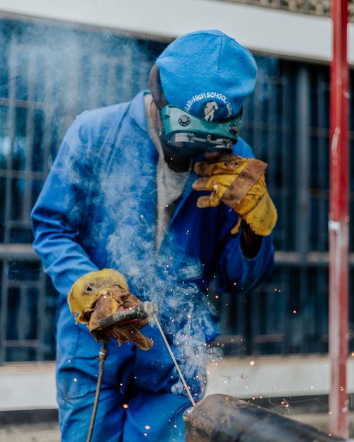 Free A welder in protective gear and gloves welding metal with sparks and smoke outdoors. Stock Photo