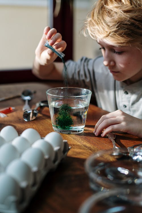 Boy Pouring Green Color Powder on Glass of Water