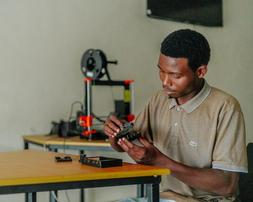 Free Focused young man assembling electronics with a 3D printer in the background. Stock Photo