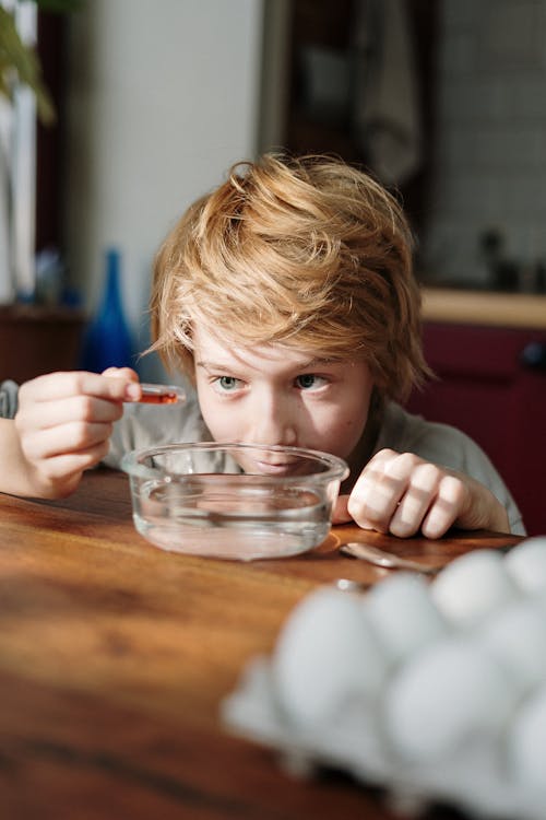 Boy Squeezing Orange Dye on Bowl with Water