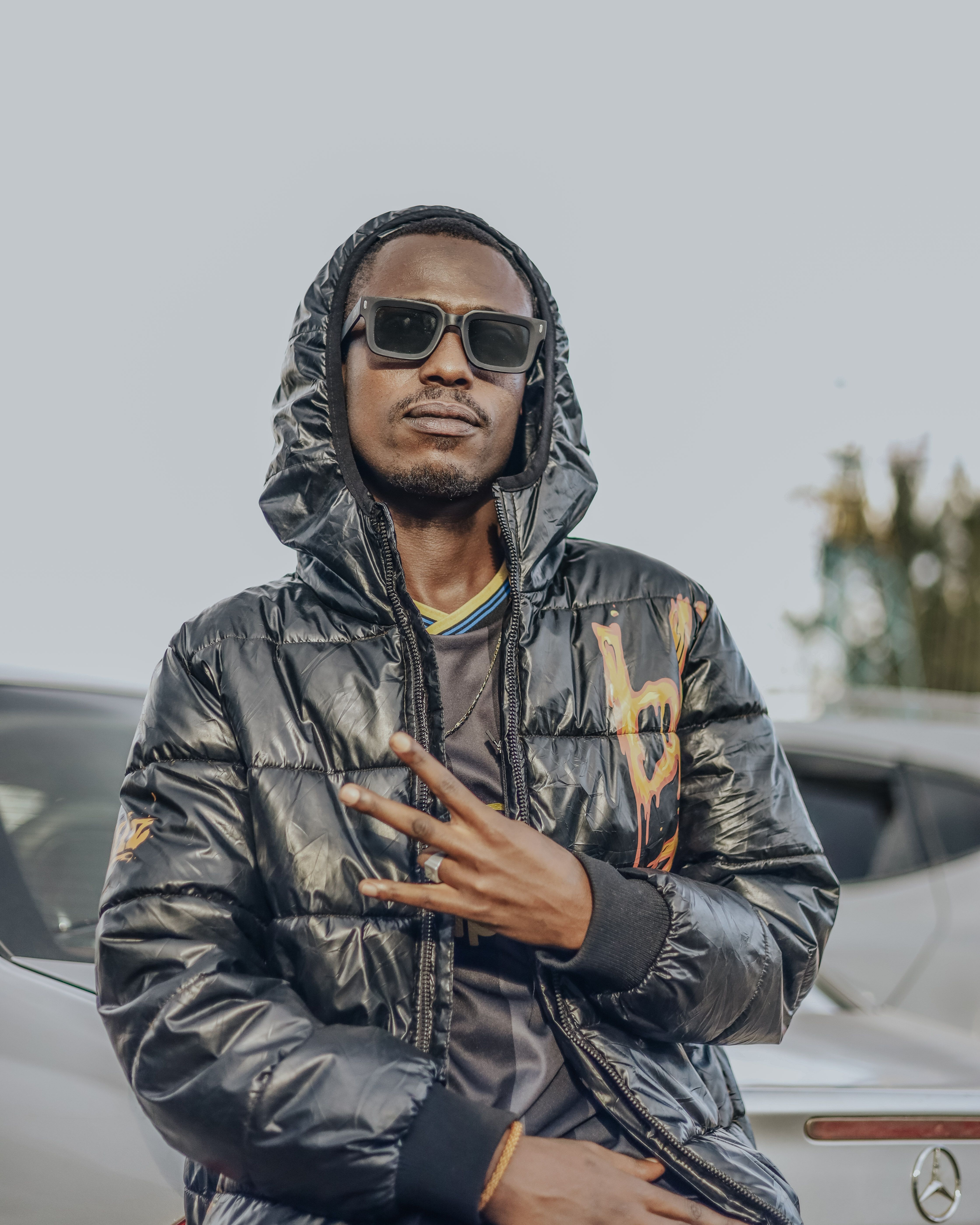Young man in urban setting wearing sunglasses and stylish jacket, exuding confidence.