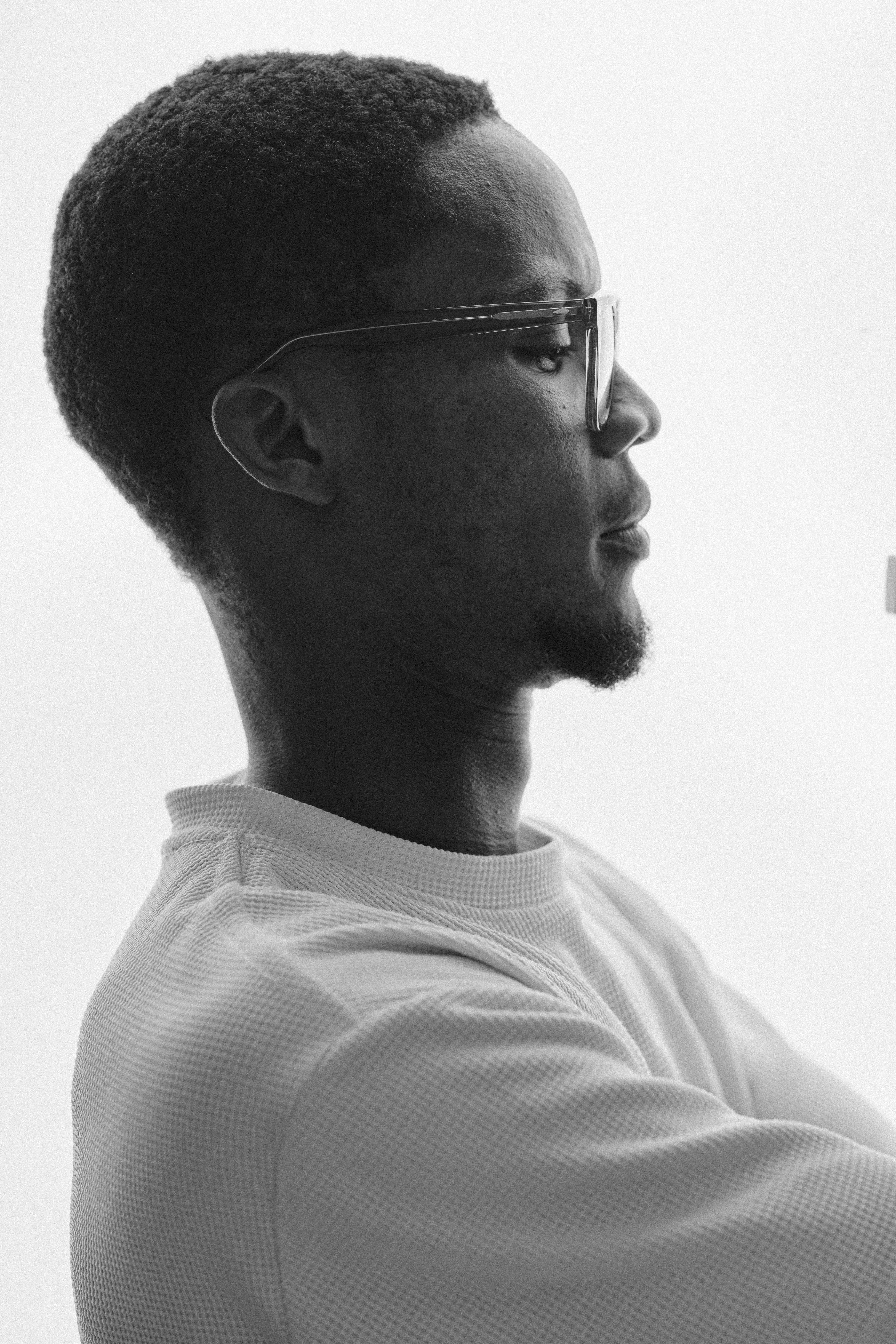 Side profile portrait of a man in glasses in a contemplative pose, captured in black and white.