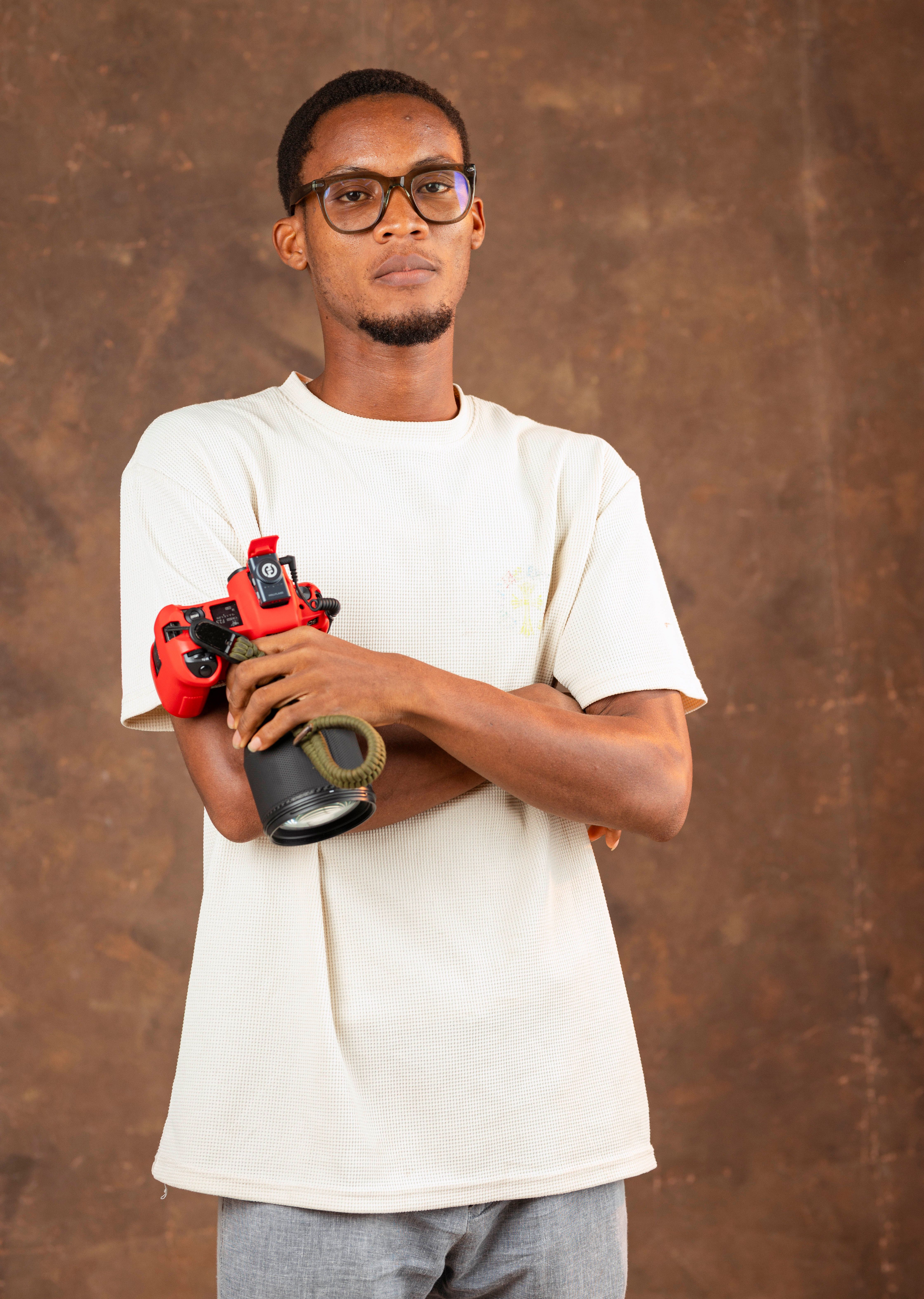 A young photographer confidently poses with a camera in a studio setting.