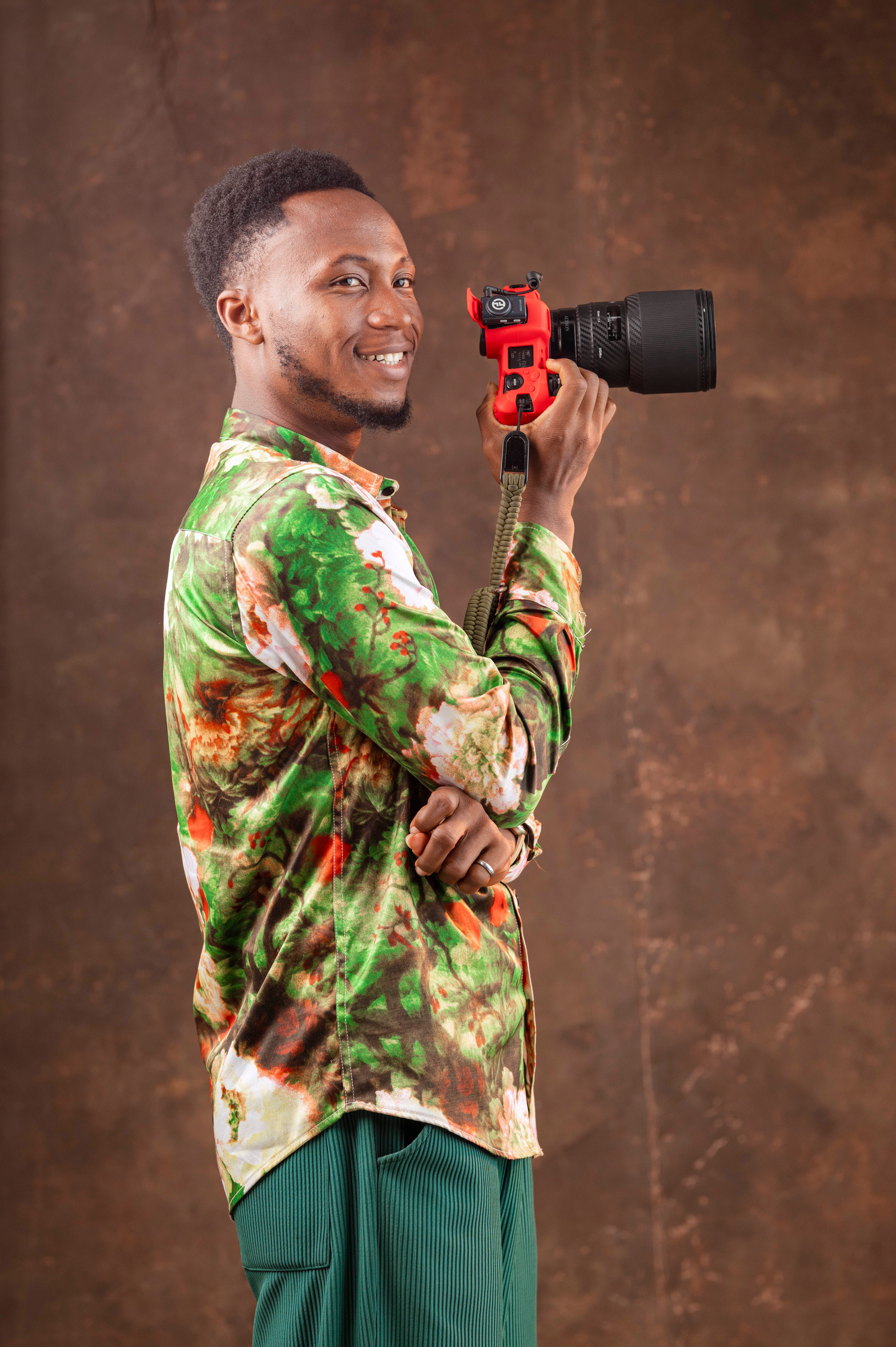 Portrait of a smiling photographer holding a camera against a textured background.
