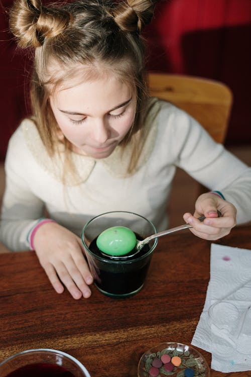 Girl in White Sweater Holding Silver Spoon Scooping Green Egg