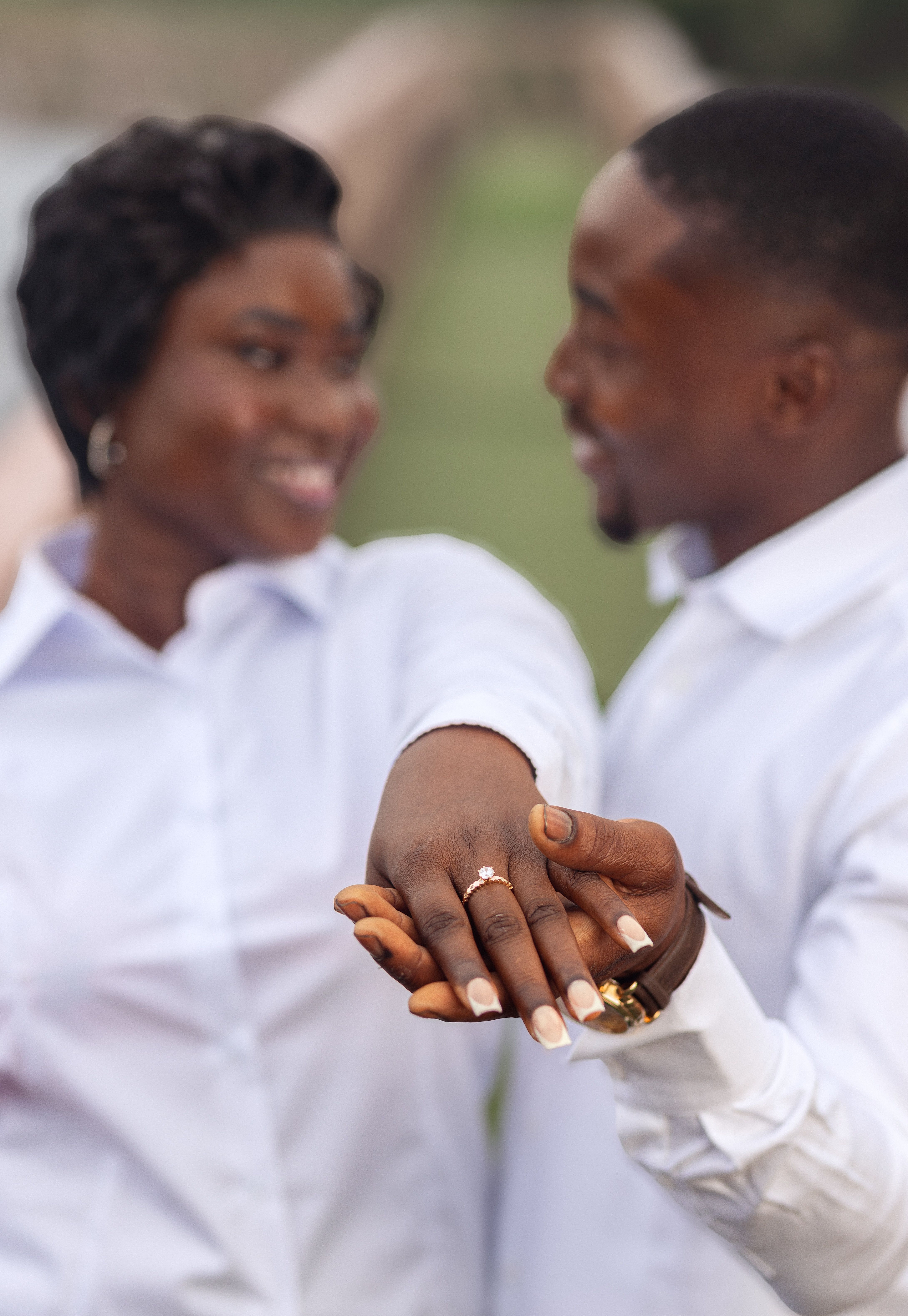 Joyful couple showing engagement ring in a serene outdoor park setting in Accra, Ghana.