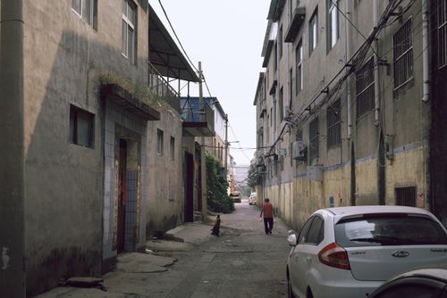 Free Urban alleyway between buildings with person walking and parked car. Stock Photo