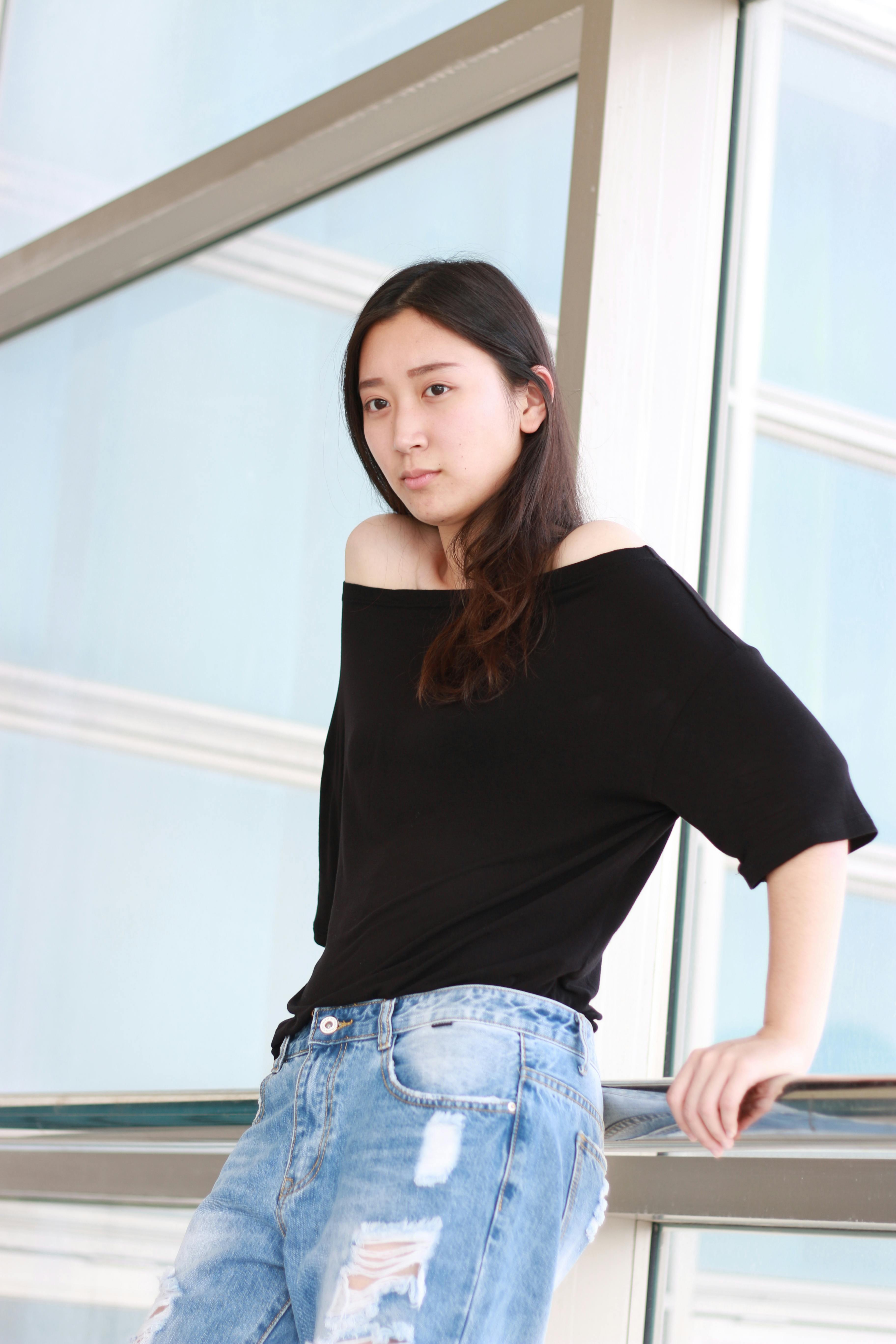 Relaxed portrait of a young woman in casual attire by a window.