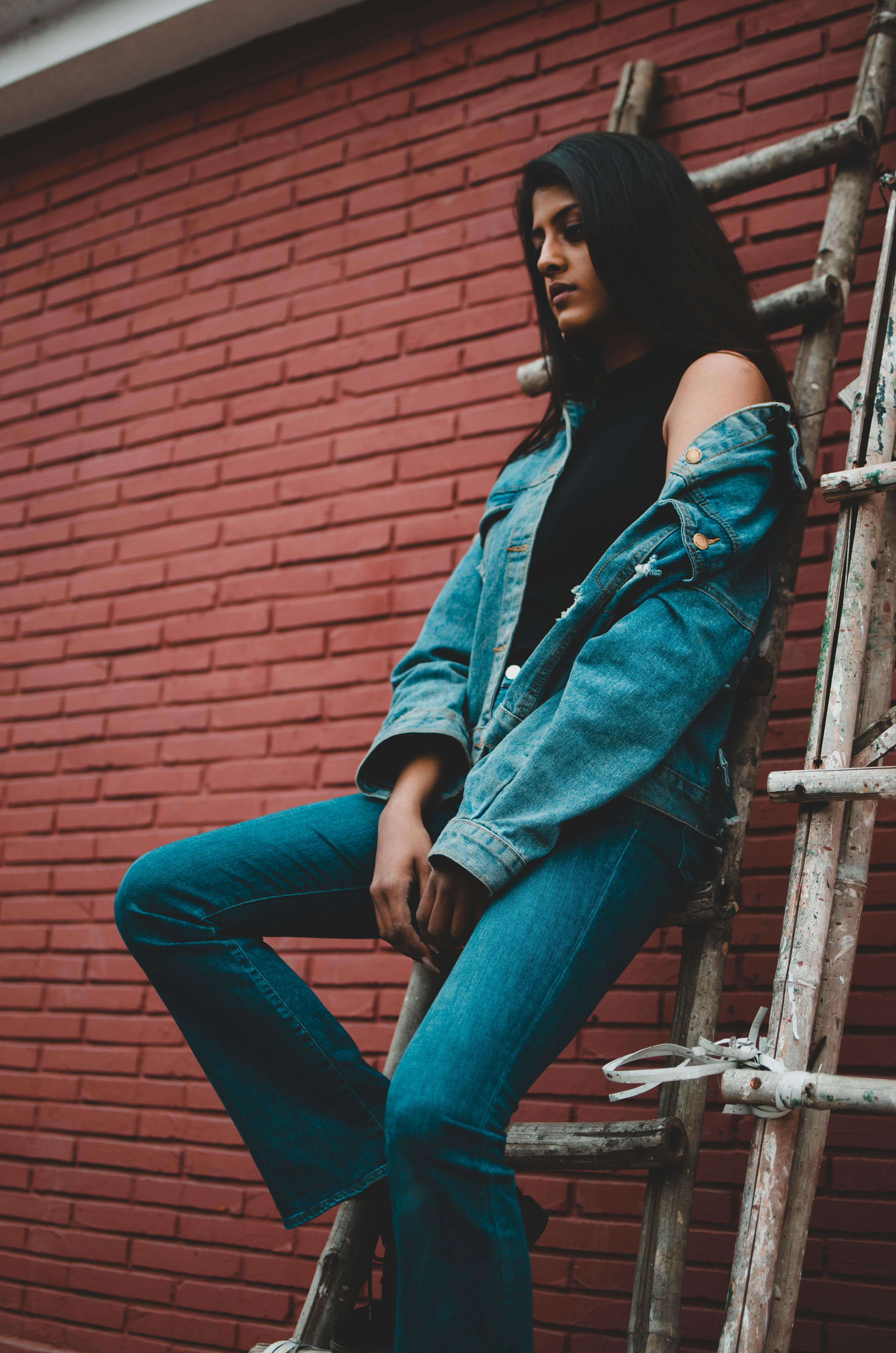 Woman in Blue Denim Jacket and Blue Denim Jeans Sitting on Wooden Ladder