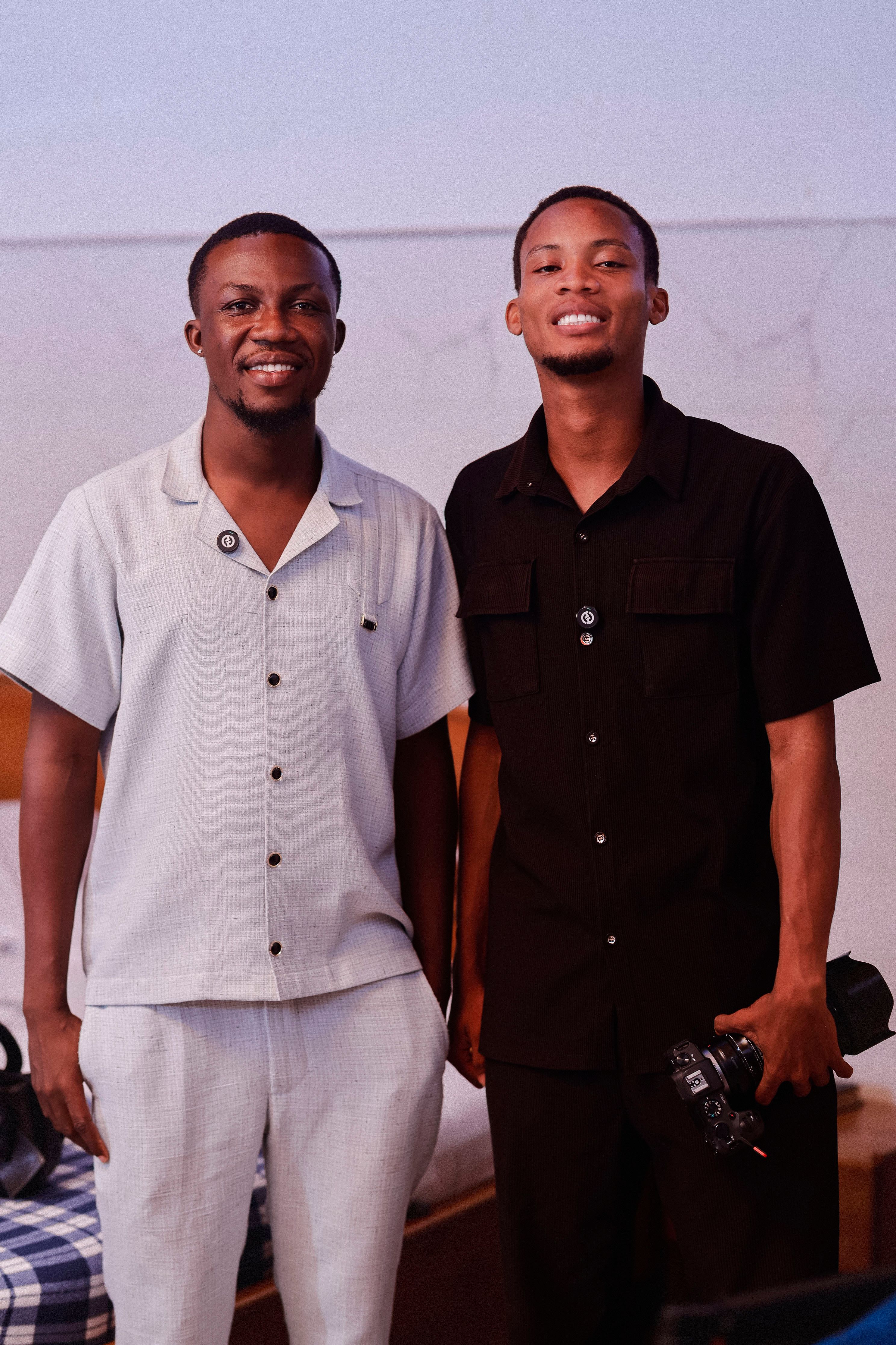 Two adult male photographers smiling and posing indoors, one holding a camera.