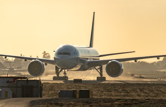 A commercial airplane prepares for takeoff on a runway during sunset with a clear sky.