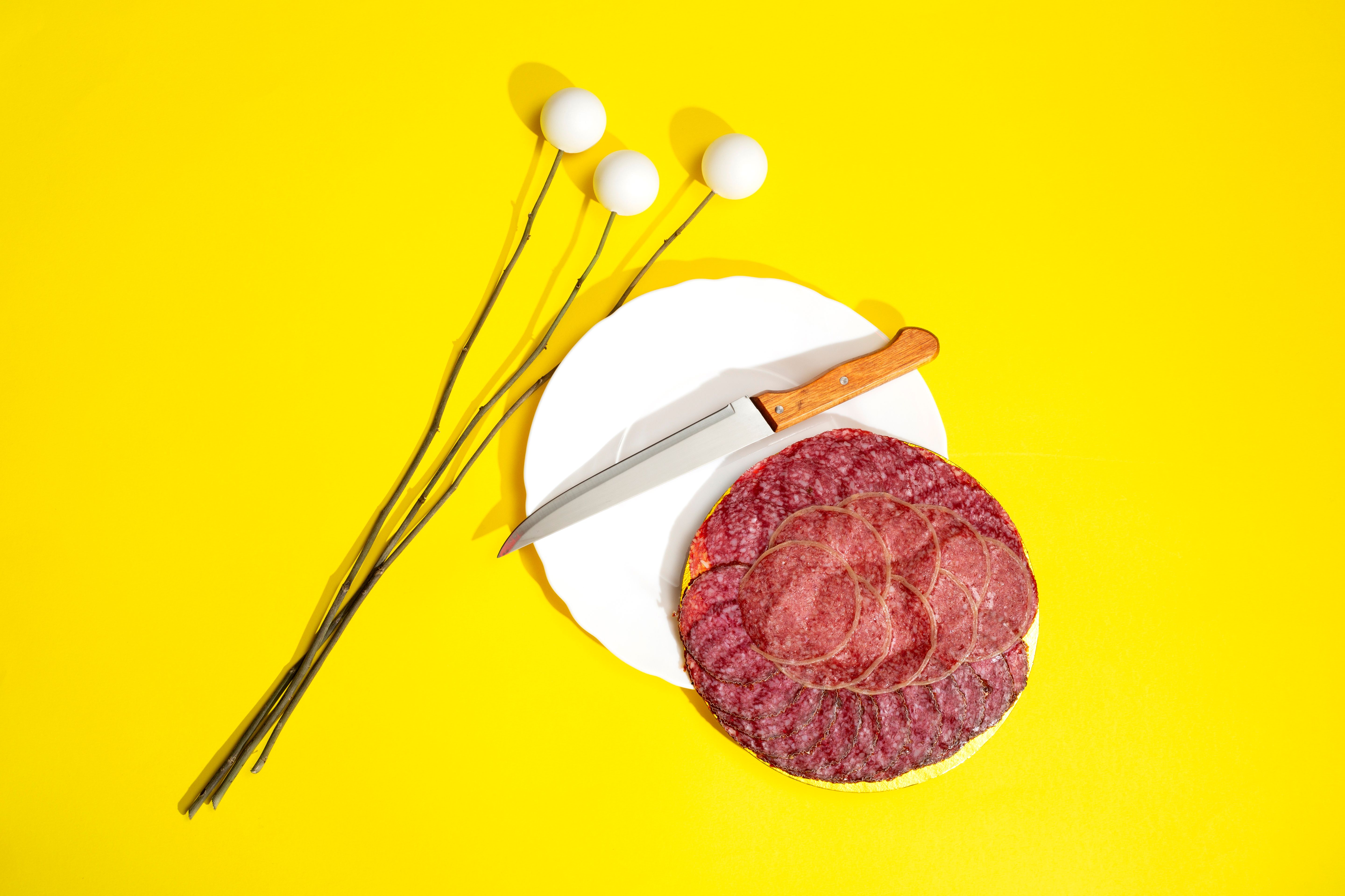 Artistic display of salami slices with knife on a bright yellow background.