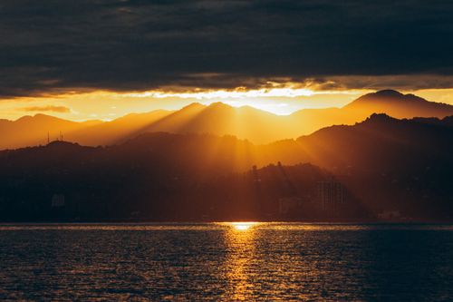 Free Captivating view of the sun setting over mountains with golden rays illuminating the sky. Stock Photo