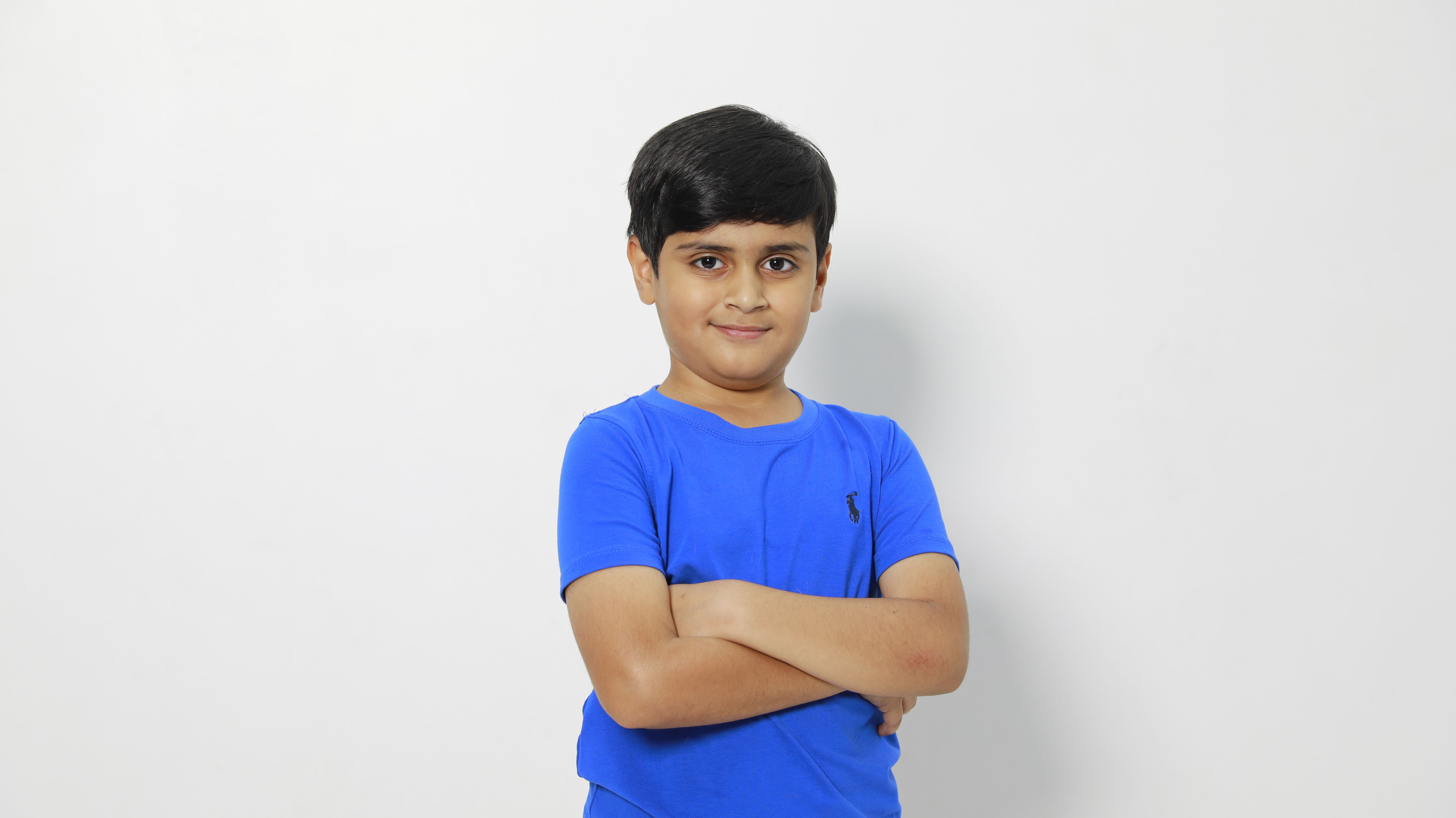 Portrait of a confident young boy in a blue shirt standing against a plain white background.