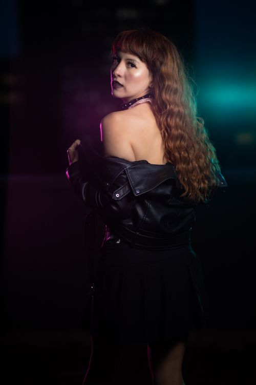 Free Woman with red hair in a leather jacket posing at night with colorful lighting. Stock Photo