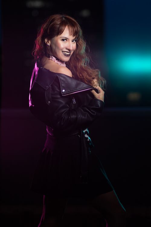 Free Portrait of a woman with red hair in a leather jacket, smiling at night. Vibrant and edgy style. Stock Photo