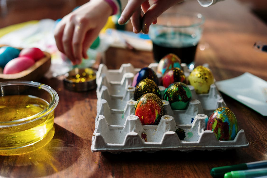 Free Hands decorating colorful Easter eggs with glitter and paint on a wooden table, capturing the festive spirit of the holiday. Stock Photo