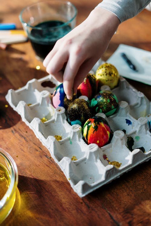 Close-up of Hand Sprinkling Glitters on Colored Eggs