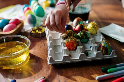 Close-up Photo of Hands Sprinkling Glitters on Colored eggs